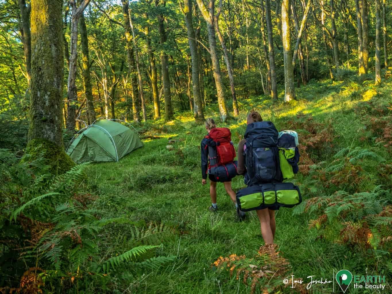 two girld walking with backpacks to a tent in the forest